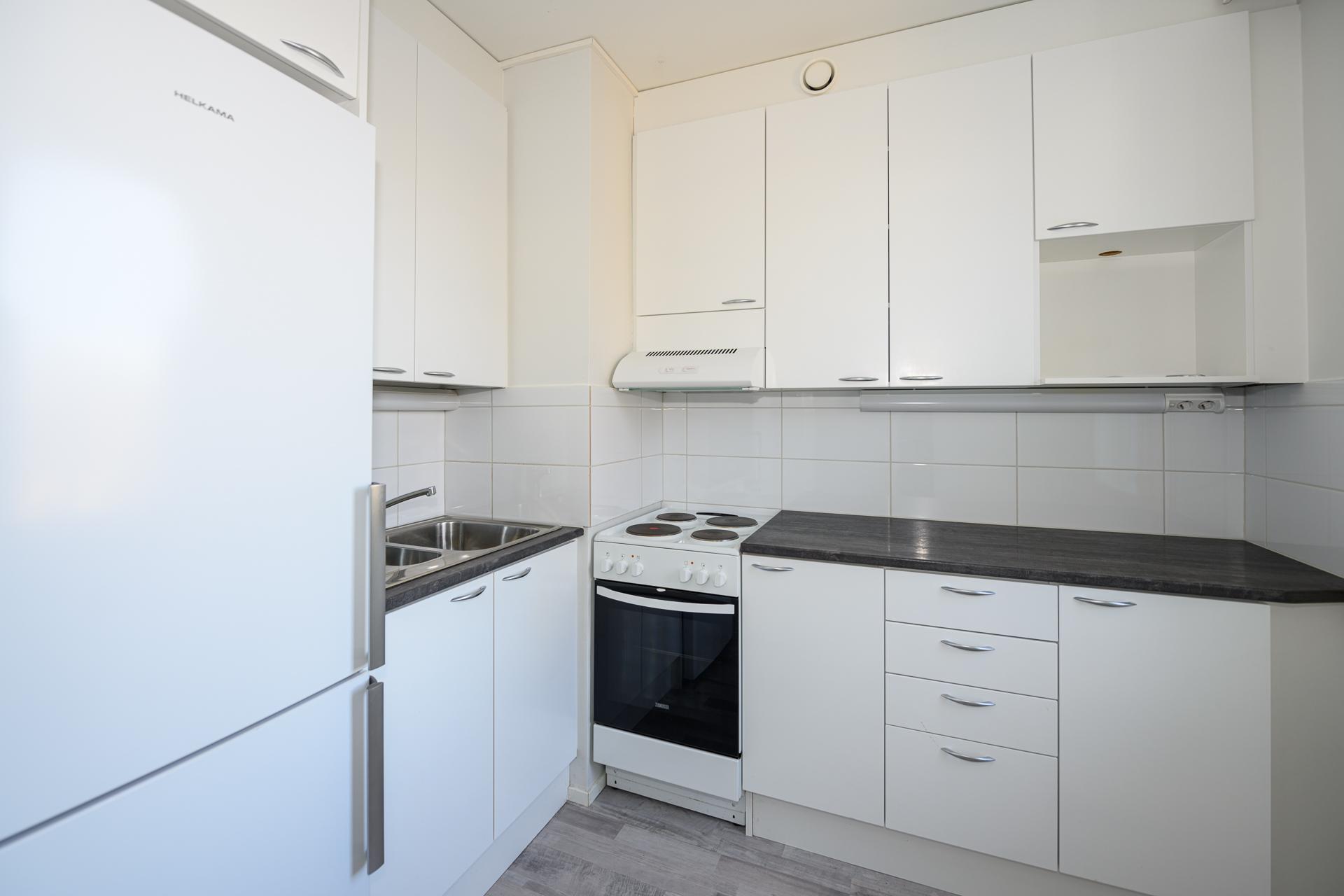 Vaaleasävyinen, kompakti keittiö, jossa on mukavasti kaapistoja ja tasotilaa.  