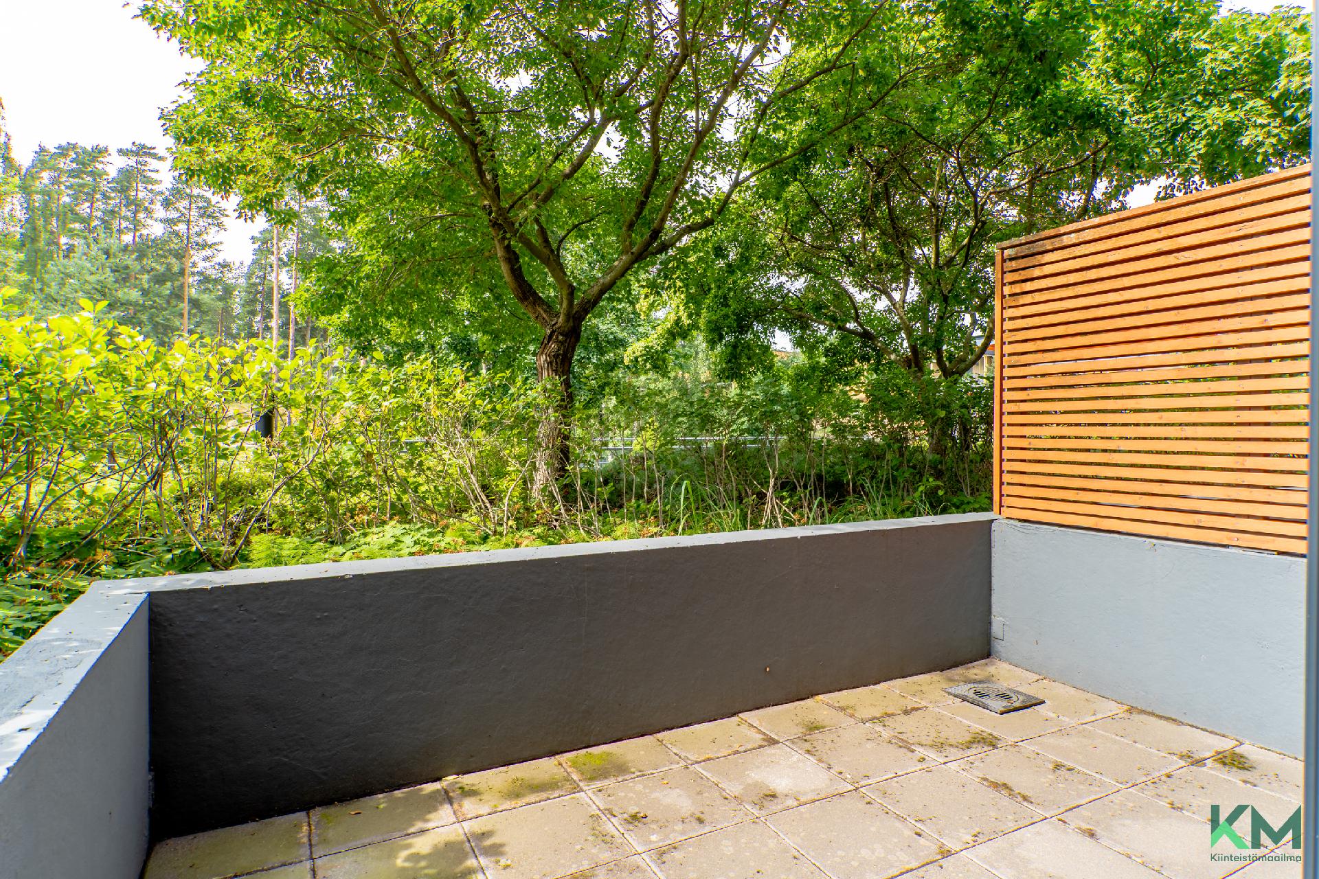 Lasitetun terassiparvekkeen edessä on avoin terassipiha, jossa on markiisi