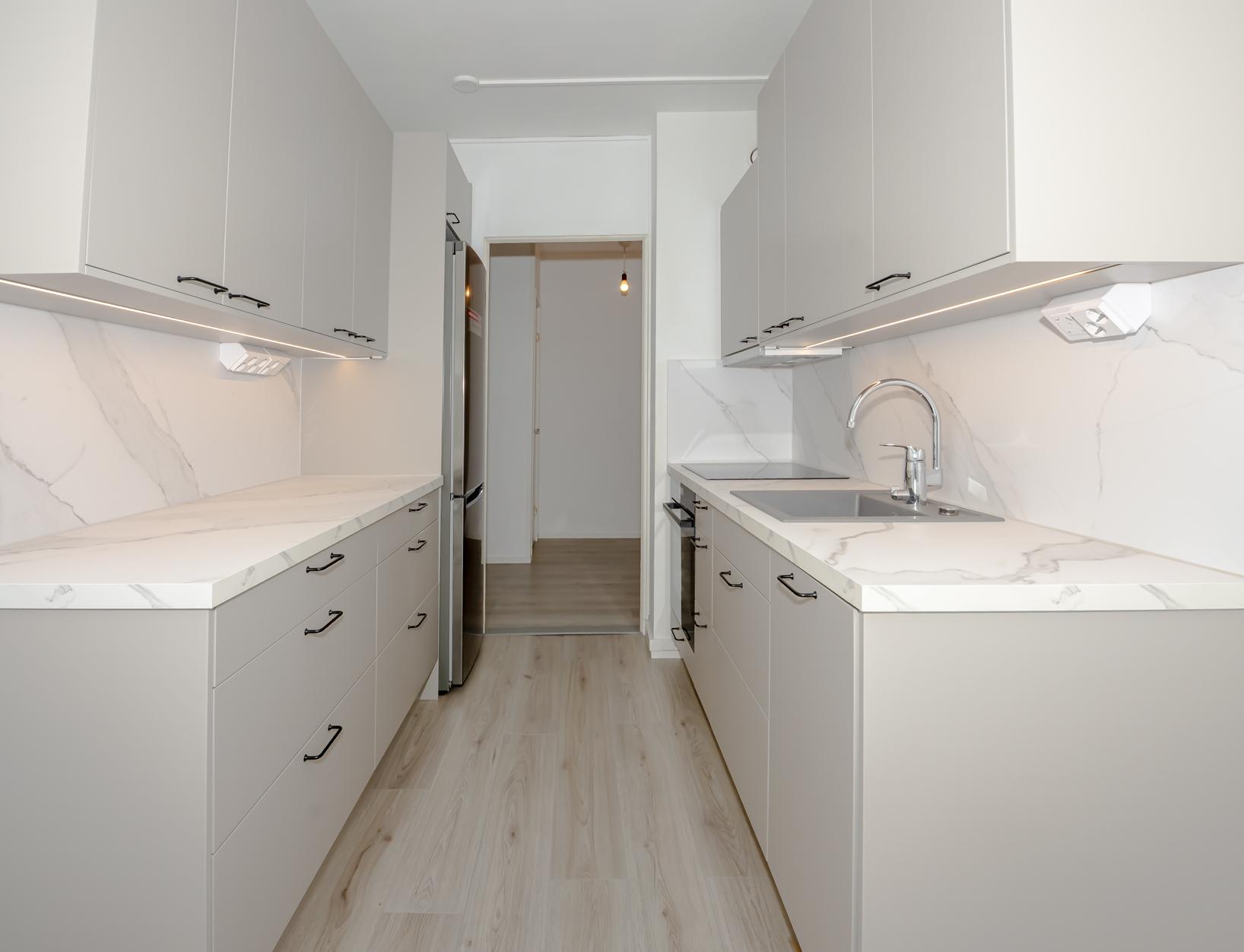 Keittiössä on kätevästi molemmin puolin kaapistoja ja tasotilaa. Oikealla puolella integroitu astianpesukone.