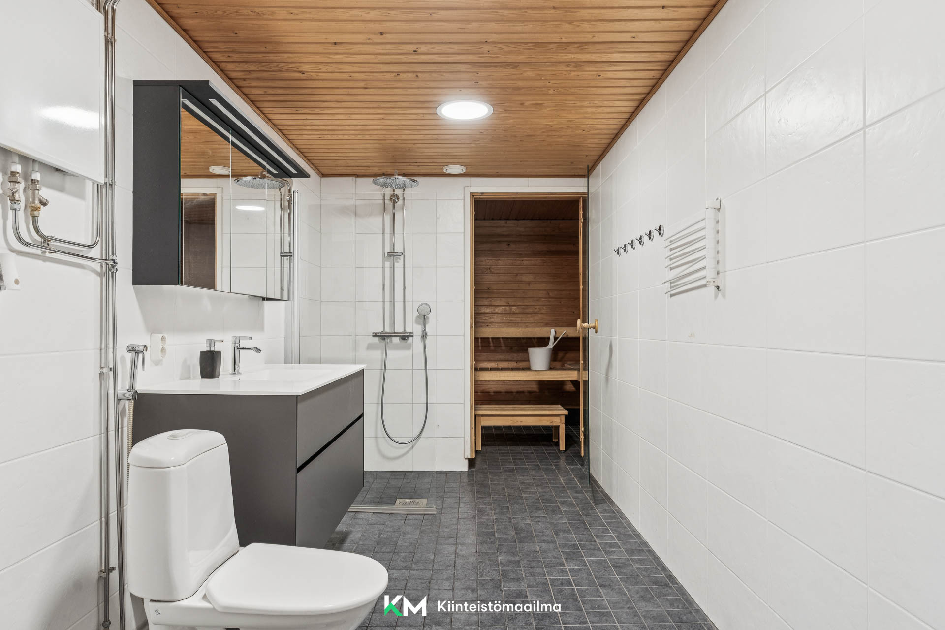 Tilava kylpyhuone sadesuihkuineen saunan yhteydessä.