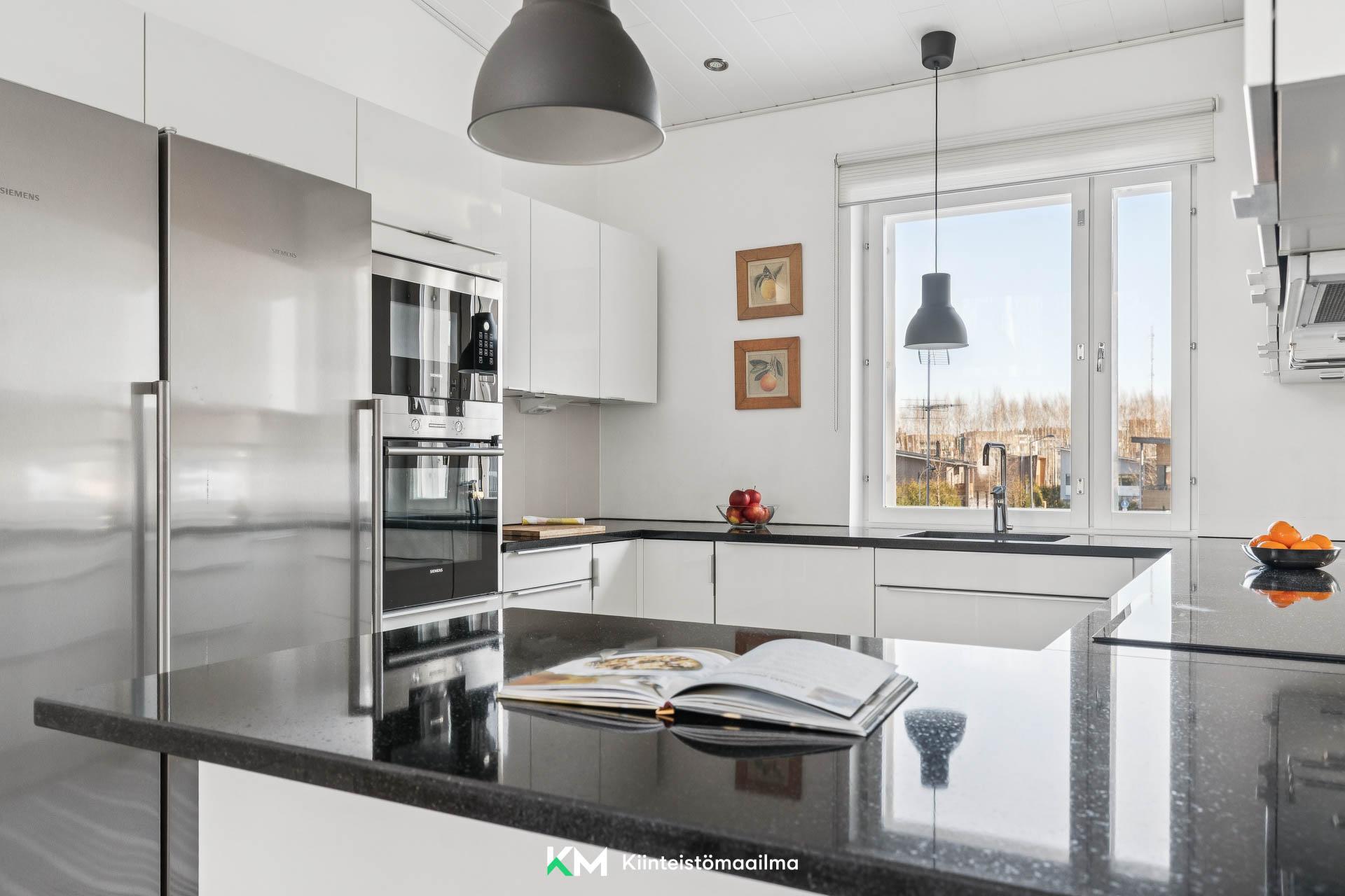 Moderni keittiö, jossa laadukkaat kodinkoneet ja tyylikkäät mustat kivitasot